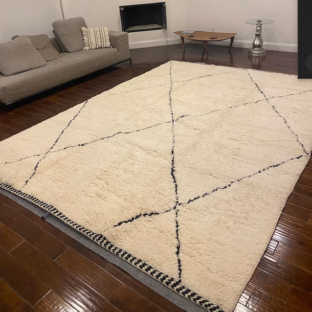 A handwoven Beni Ourain rug being cleaned with a vacuum cleaner.